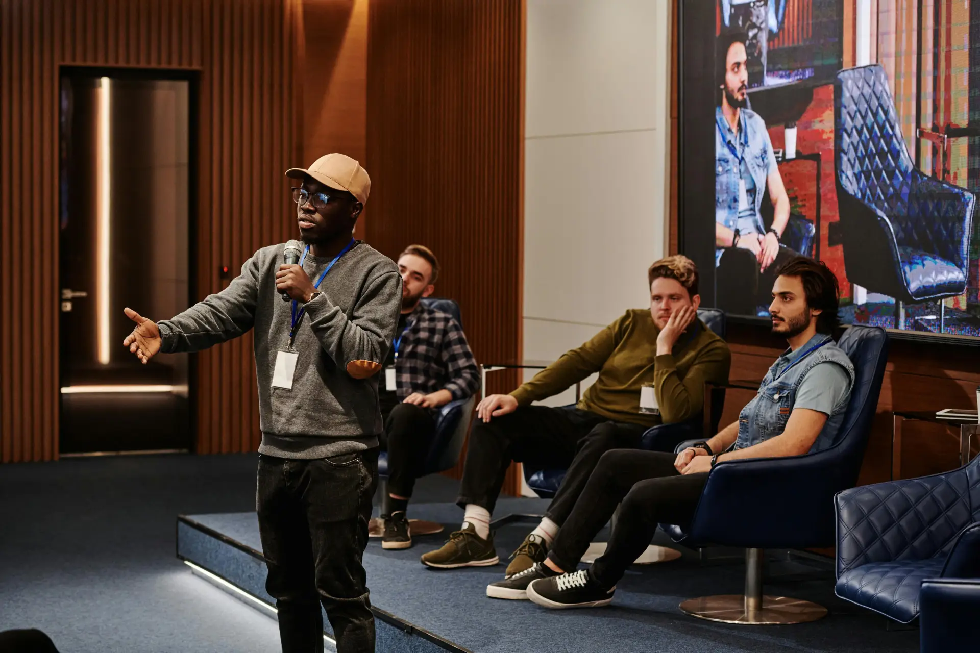 A group of diverse men engaging in a business conference with a speaker holding a microphone.
