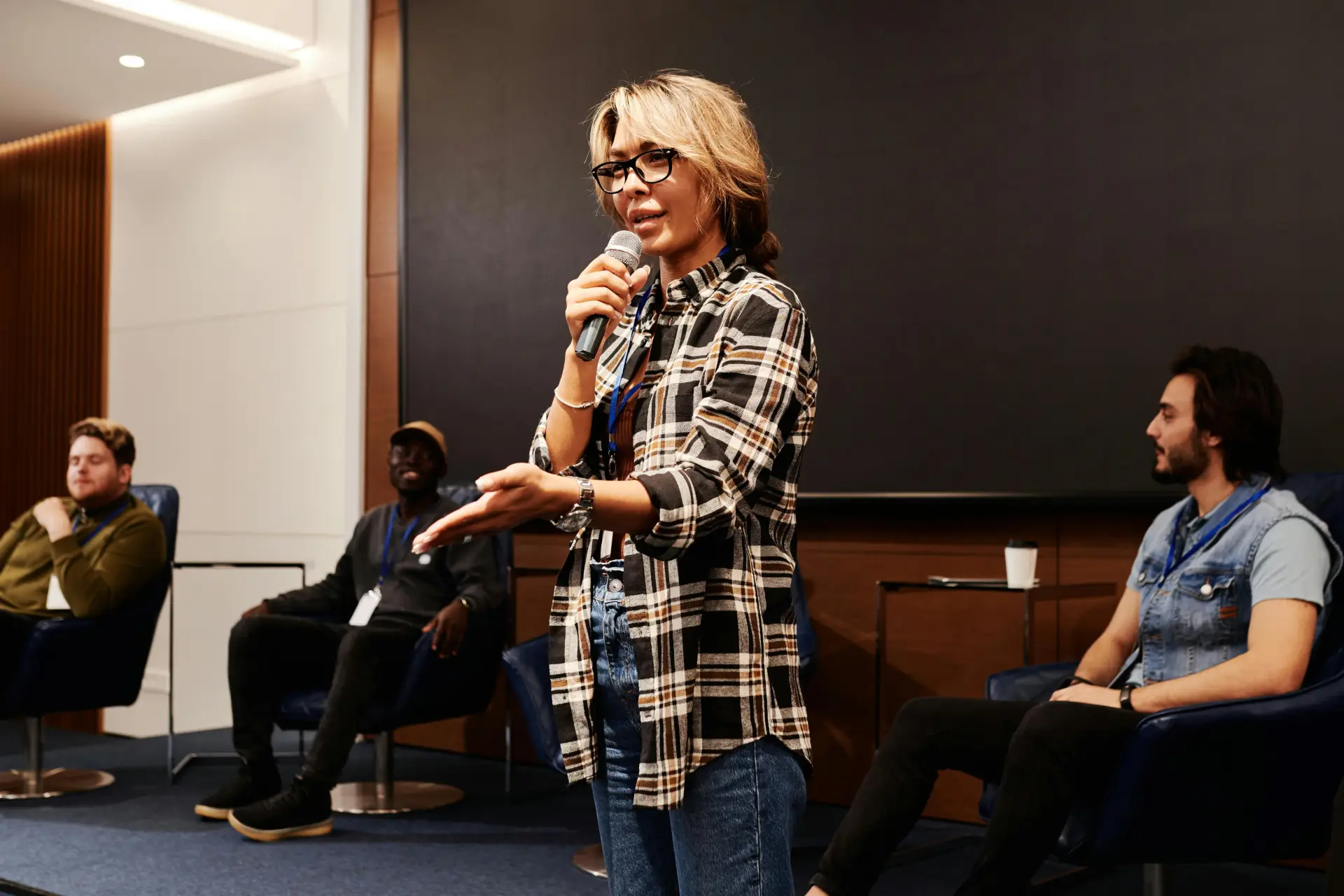 A group of diverse men engaging in a business conference with a speaker holding a microphone.
