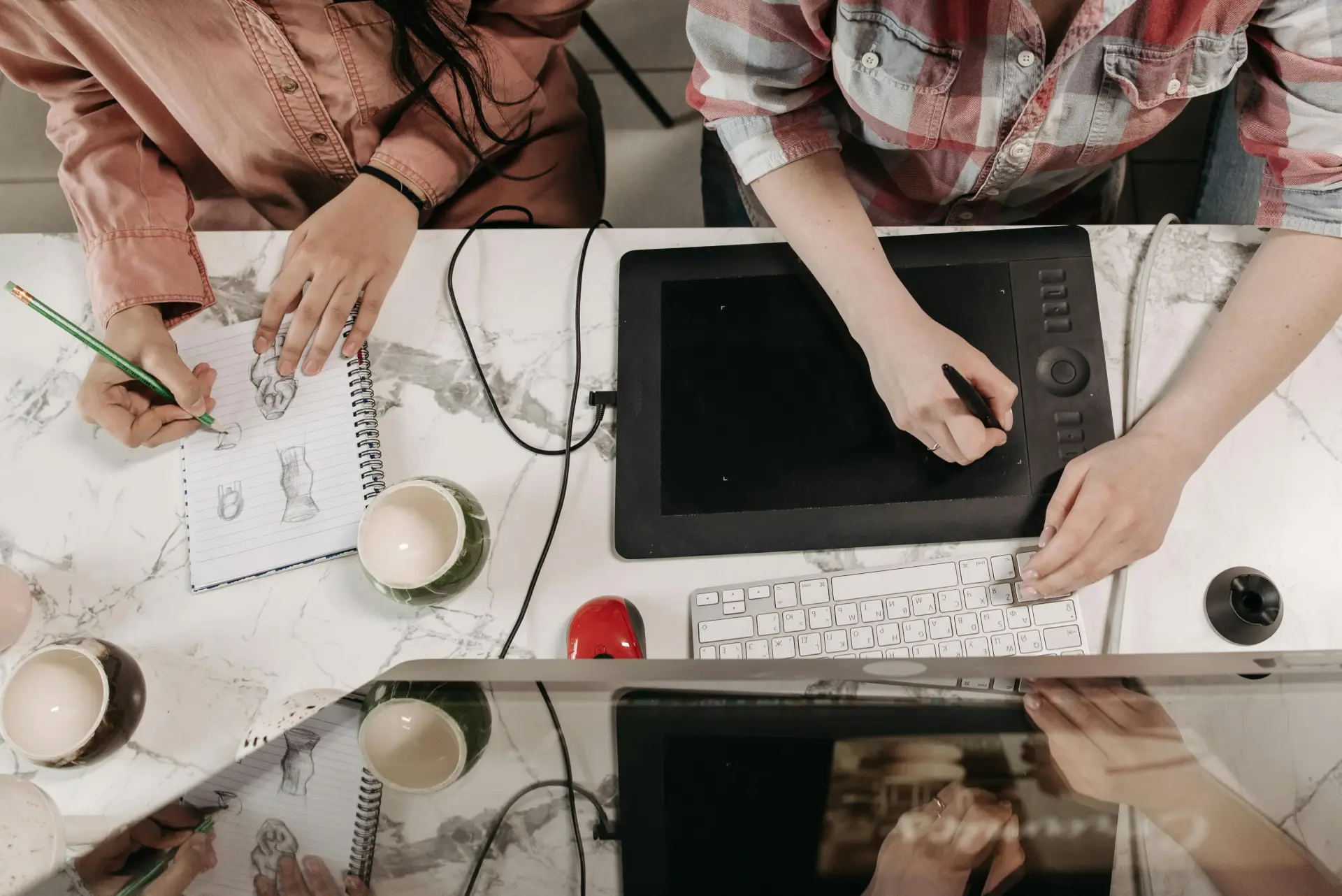 Two people collaborating with a digital tablet and sketches at a marble table.
