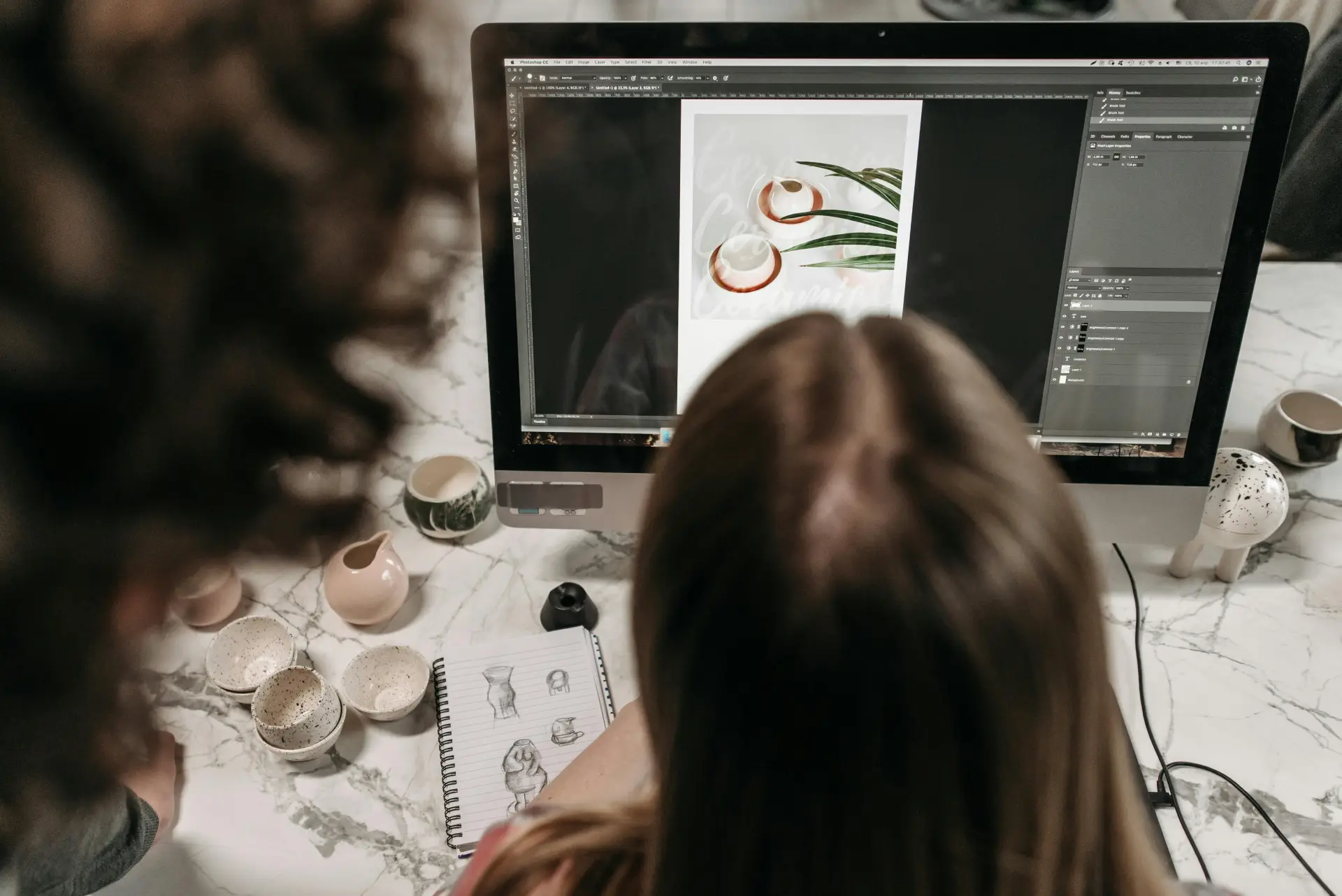 Two people collaborate on photo editing using Adobe Photoshop in a studio setting.

