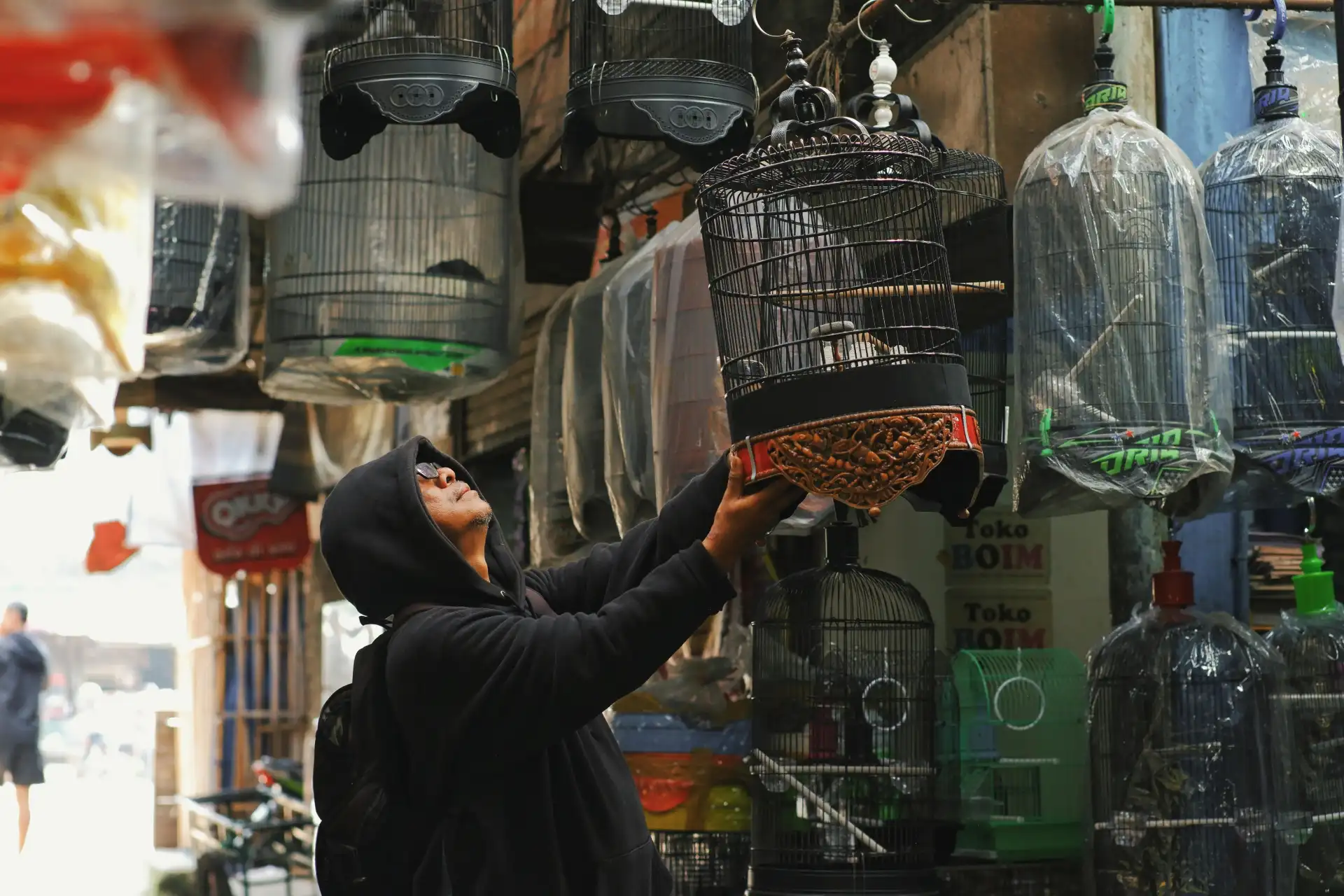 A man examines bird cages in a lively market in Bandung, Indonesia, showcasing local culture.
