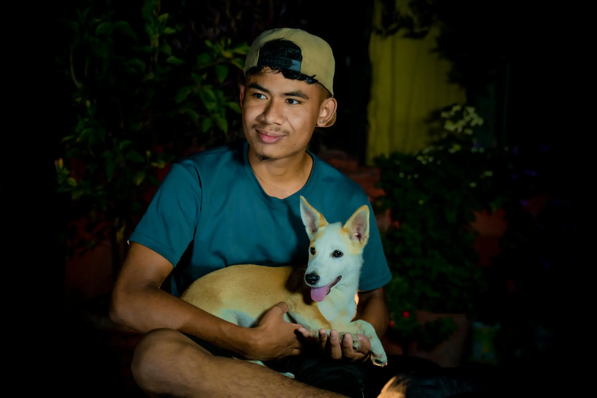 Portrait of a young man sitting outdoors with his dog, smiling at night.
