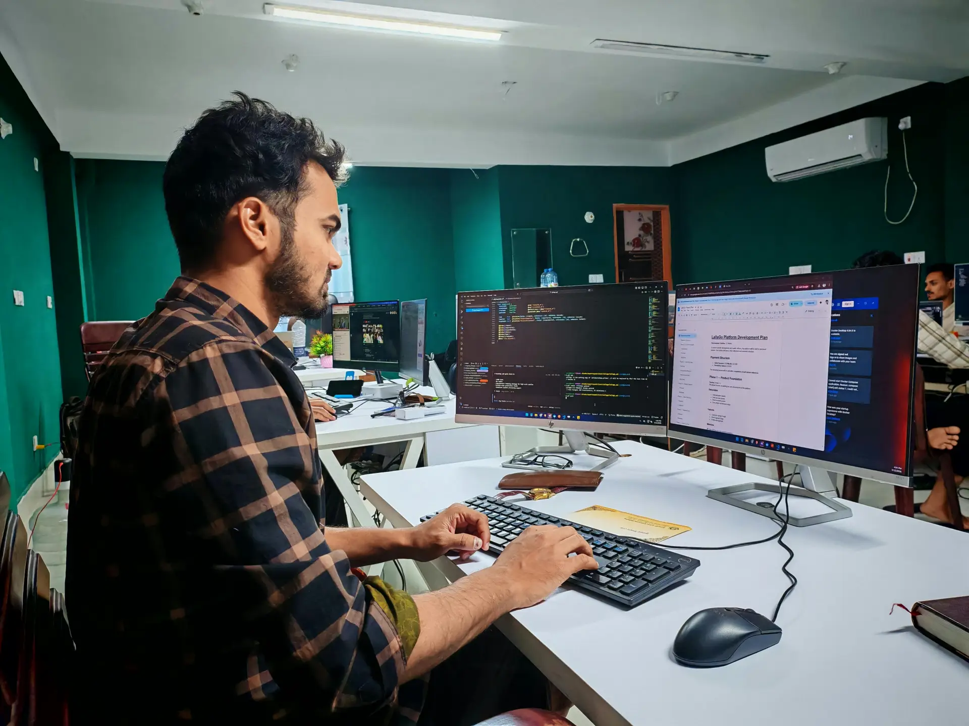 A software developer working on code at a dual monitor setup in a modern office.
